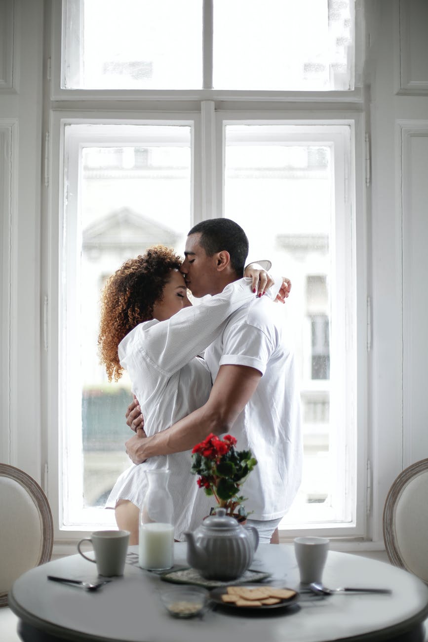 couple hugging and kissing while standing near window at home